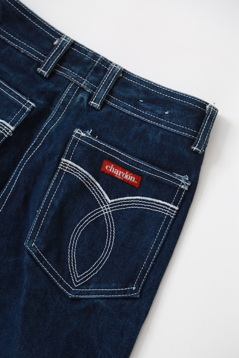 May include: Dark blue denim jeans with white stitching detail. The back pocket has a red label with the text "chardon paris" in white.