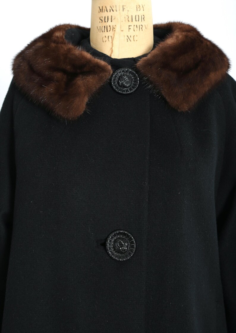 May include: A black coat with a brown fur collar and two decorative black buttons. The coat is made of a dark fabric and has a classic design, suitable for cold weather.