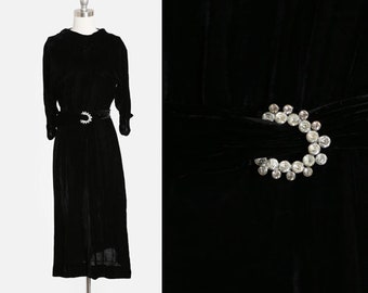 May include: A black velvet dress with a long sleeve and a rhinestone belt buckle.