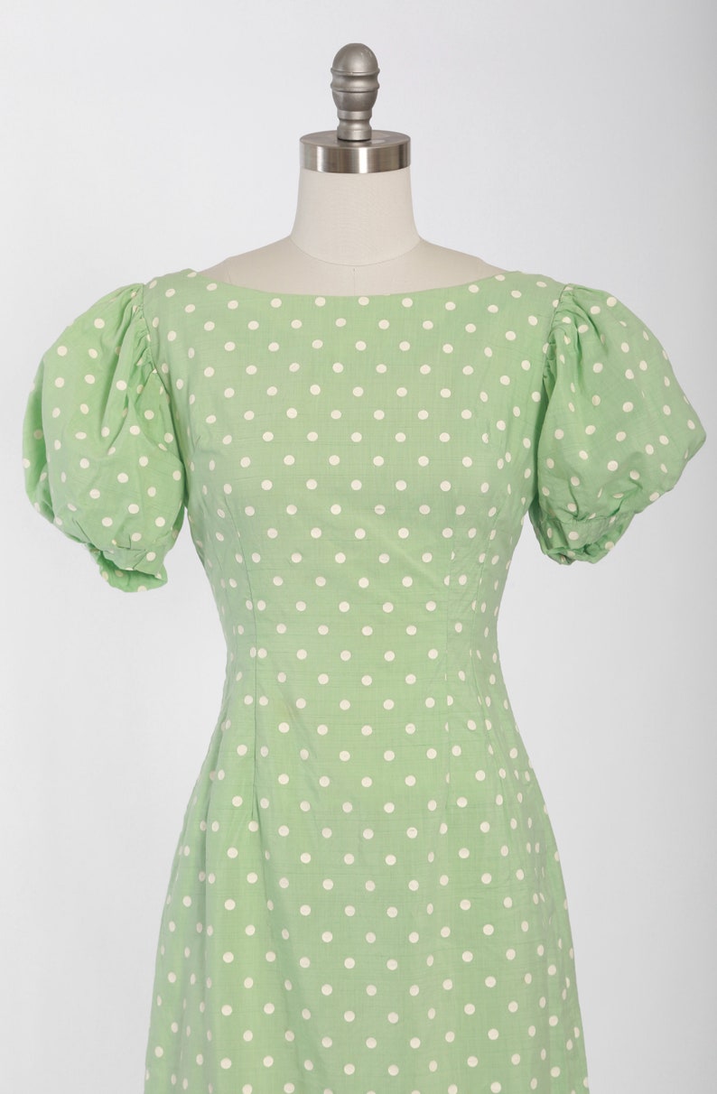 May include: A green dress with white polka dots and short puffed sleeves.