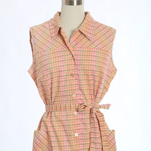May include: A sleeveless, button-down dress with a pink, green and yellow plaid pattern. The dress has a tie belt and two patch pockets.