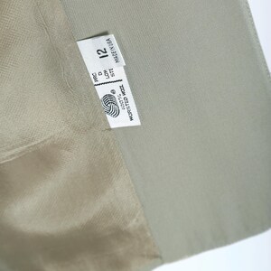 K&ouml;nnte beinhalten: Nahaufnahme eines hellgr&uuml;nen Blazers mit einem Etikett mit der Aufschrift "Made in USA" und der Gr&ouml;&szlig;e "12". Das Etikett enth&auml;lt auch ein Wollsymbol und die Worte "100% Worsted Wool". Das Innenfutter des Blazers ist hellbeige.