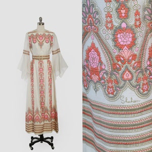 May include: A white maxi dress with a floral print and bell sleeves. The dress has a fitted bodice and a flowing skirt. The dress is made of a lightweight fabric and is perfect for summer.