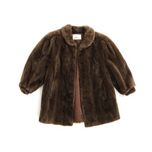 May include: A brown faux fur coat with a rounded collar and three-quarter sleeves. The coat is open at the front, revealing a brown lining. The coat is a vintage style.