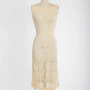 Op de afbeelding: Een mouwloze, cr&egrave;mekleurige kanten jurk met een getailleerd lijfje en een licht uitlopende rok. De jurk is op een mannequin.