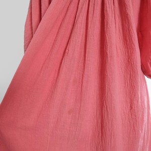 K&ouml;nnte beinhalten: Ein korallfarbenes Kleid mit strukturiertem Stoff und gerafftem Ausschnitt. Das Kleid hat Dreiviertel&auml;rmel und eine flie&szlig;ende Silhouette. Der Stoff scheint leicht zu sein, geeignet f&uuml;r w&auml;rmeres Wetter. Das Kleid ist einfarbig mit einem schlichten, eleganten Design.