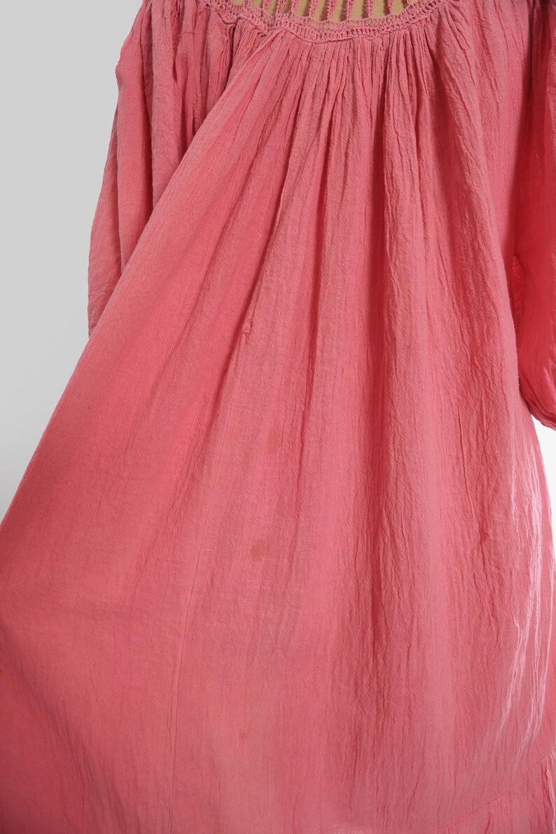 K&ouml;nnte beinhalten: Ein korallfarbenes Kleid mit strukturiertem Stoff und gerafftem Ausschnitt. Das Kleid hat Dreiviertel&auml;rmel und eine flie&szlig;ende Silhouette. Der Stoff scheint leicht zu sein, geeignet f&uuml;r w&auml;rmeres Wetter. Das Kleid ist einfarbig mit einem schlichten, eleganten Design.