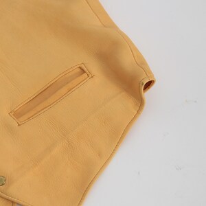 May include: A yellow leather vest with a pocket on the front. The vest has a pointed collar and a button closure.