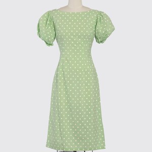 May include: A green dress with white polka dots and short puff sleeves. The dress is fitted at the waist and has a midi length.