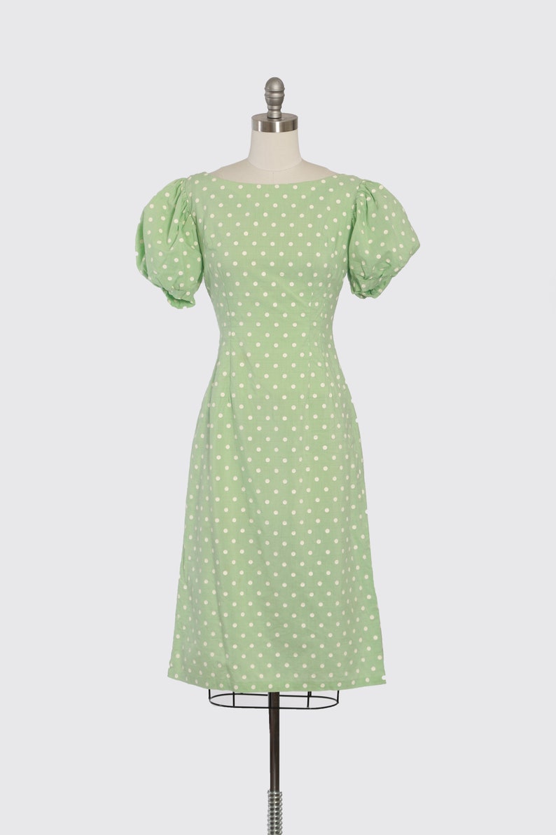 May include: A green dress with white polka dots and short puff sleeves. The dress is fitted at the waist and has a midi length.