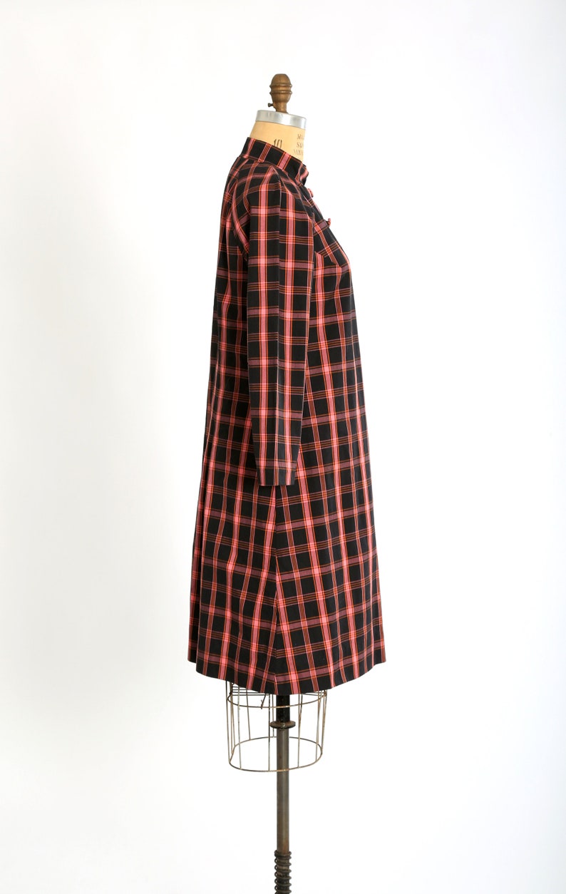 May include: A black and pink plaid dress with a mandarin collar and long sleeves. The dress is on a mannequin.