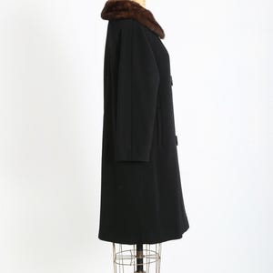 May include: A vintage black coat with a brown fur collar. The coat is displayed on a mannequin and features a classic design with a button closure. The coat's length extends to the mid-calf, offering a timeless silhouette.