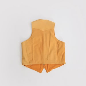 May include: A yellow suede vest with a pointed collar and a zipper closure.