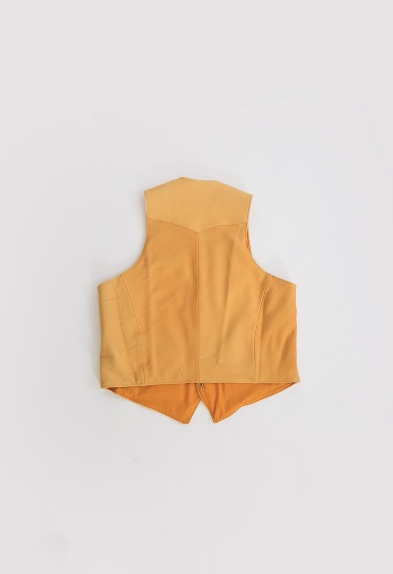 May include: A yellow suede vest with a pointed collar and a zipper closure.