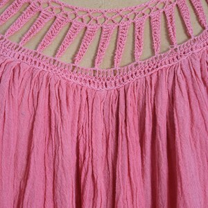 K&ouml;nnte beinhalten: Nahaufnahme eines pinkfarbenen Oberteils mit einem H&auml;kel-Ausschnitt. Das Oberteil hat einen gerafften, strukturierten Stoff, und das H&auml;keldesign weist vertikale und horizontale Linien auf. Die Farbe ist ein leuchtendes, einfarbiges Pink.