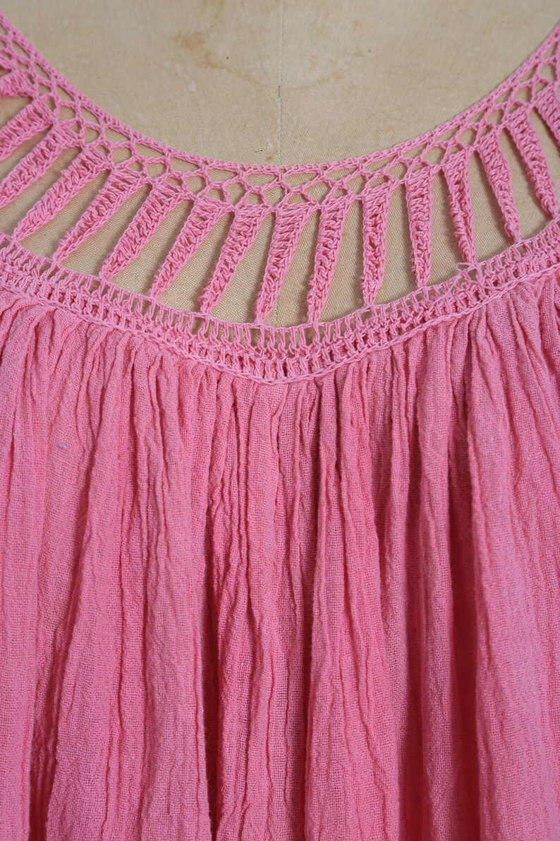 K&ouml;nnte beinhalten: Nahaufnahme eines pinkfarbenen Oberteils mit einem H&auml;kel-Ausschnitt. Das Oberteil hat einen gerafften, strukturierten Stoff, und das H&auml;keldesign weist vertikale und horizontale Linien auf. Die Farbe ist ein leuchtendes, einfarbiges Pink.