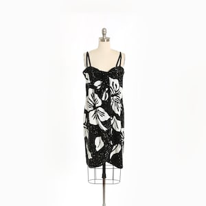 May include: A black sequined dress with a white floral pattern. The dress has thin straps and a fitted silhouette.