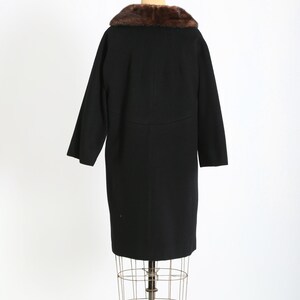 May include: A vintage black coat with a brown fur collar, displayed on a wire dress form. The coat has long sleeves and a knee-length hem. The fur collar adds a touch of luxury to the classic design.