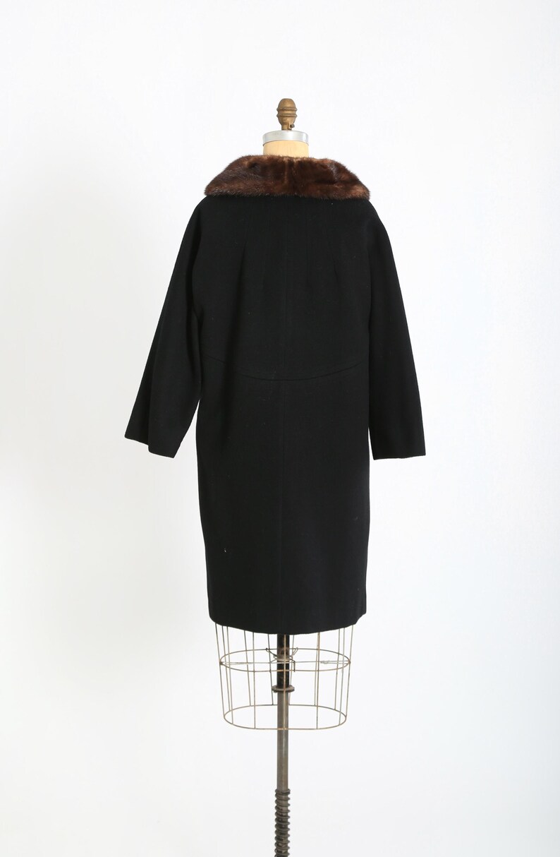 May include: A vintage black coat with a brown fur collar, displayed on a wire dress form. The coat has long sleeves and a knee-length hem. The fur collar adds a touch of luxury to the classic design.