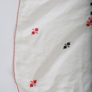 May include: White linen tablecloth with a red embroidered border and black and red embroidered floral designs.