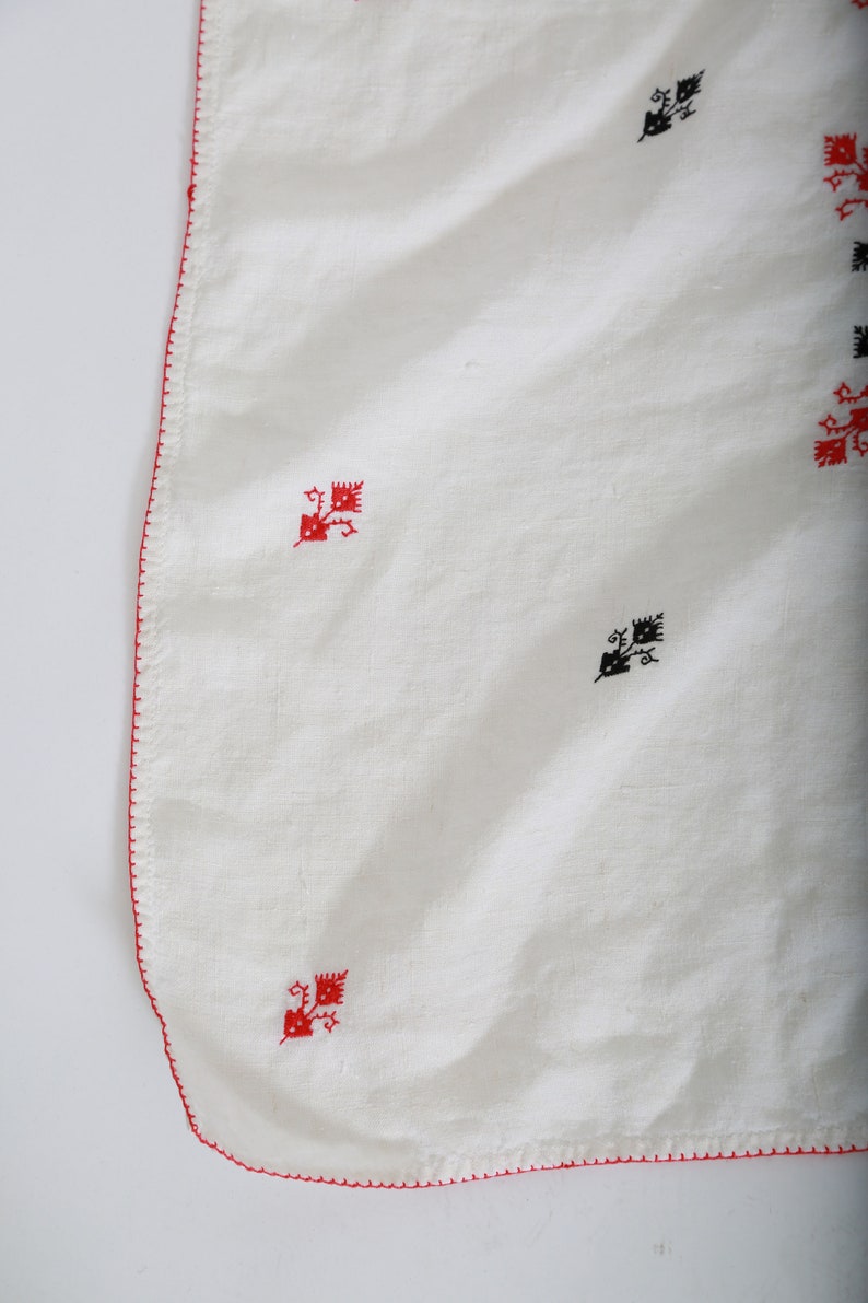 May include: White linen tablecloth with a red embroidered border and black and red embroidered floral designs.