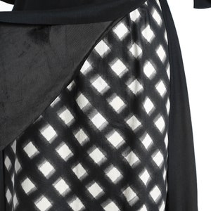 Puede incluir: Vestido de cuadros negros y blancos con una superposici&oacute;n negra. La superposici&oacute;n est&aacute; drapeada sobre el vestido y atada a la cintura.