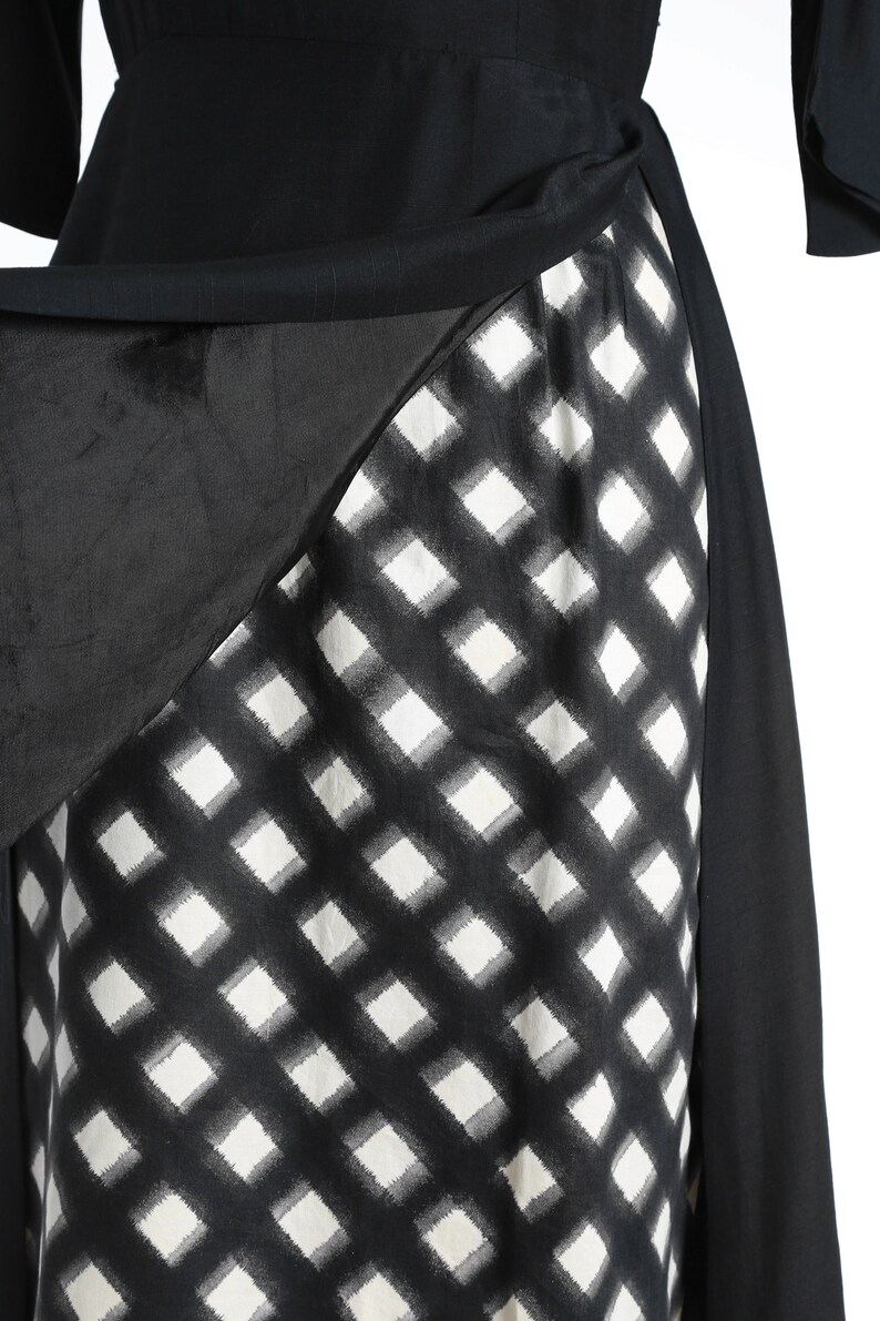 Puede incluir: Vestido de cuadros negros y blancos con una superposici&oacute;n negra. La superposici&oacute;n est&aacute; drapeada sobre el vestido y atada a la cintura.