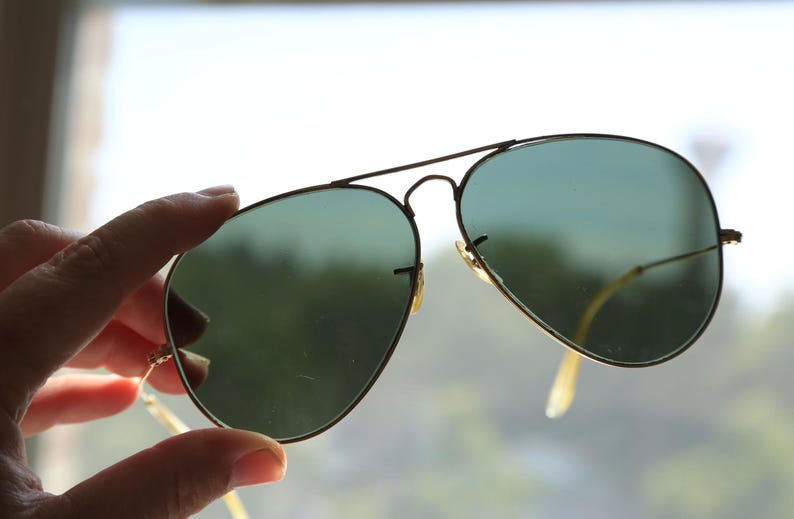 May include: Aviator sunglasses featuring a thin gold-tone metal frame and teardrop-shaped green tinted lenses. The eyewear includes a double bridge design across the top and slender metal temples with curved ends for a secure fit over the ears.