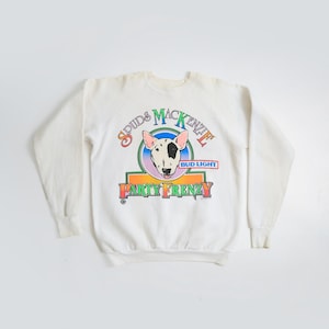 May include: White crewneck sweatshirt featuring a colorful graphic of a bull terrier dog with the text "Spuds MacKenzie" and "Party Frenzy". The Bud Light logo is also present. The sweatshirt has long sleeves and a relaxed fit.