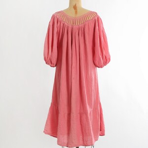 K&ouml;nnte beinhalten: Ein korallrosa Kleid im Vintage-Stil mit einem Rundhalsausschnitt und kurzen, gepufften &Auml;rmeln. Das Kleid hat einen Stufenrock und wird auf einer Schaufensterpuppe pr&auml;sentiert. Der Stoff wirkt leicht und flie&szlig;end.