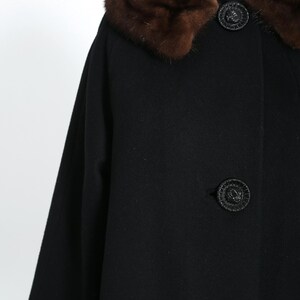 May include: A black vintage coat with a brown fur collar and decorative buttons. The coat has a classic design with a mid-length cut and three-quarter sleeves. The buttons are round and textured.