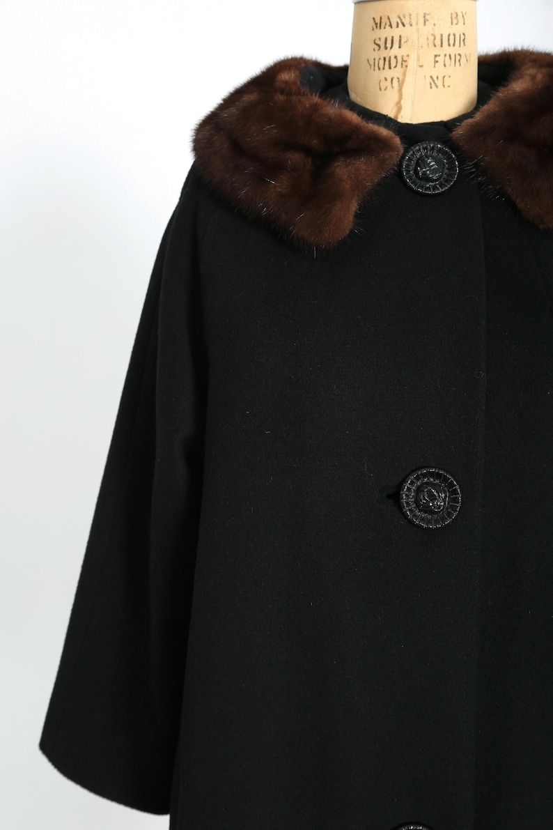 May include: A black vintage coat with a brown fur collar and decorative buttons. The coat has a classic design with a mid-length cut and three-quarter sleeves. The buttons are round and textured.