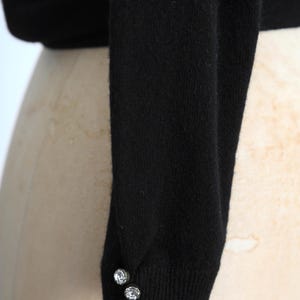May include: Black long-sleeved sweater with two silver buttons on the cuff.