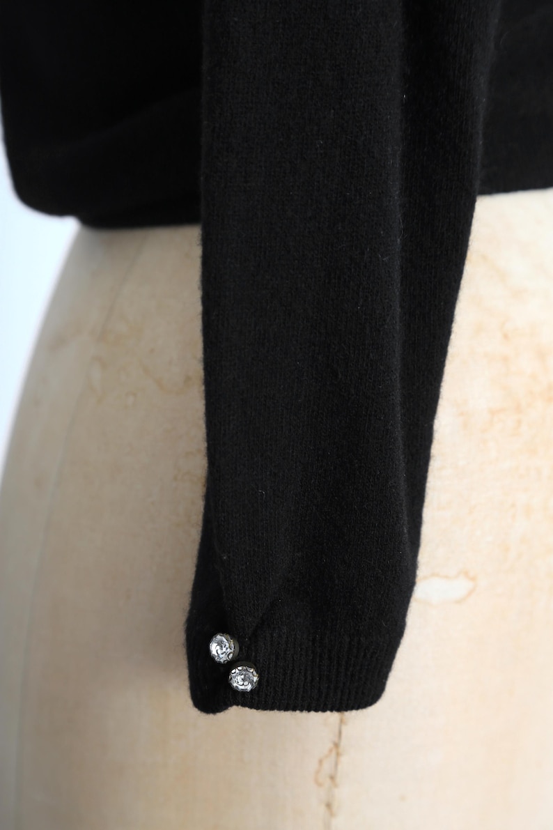 May include: Black long-sleeved sweater with two silver buttons on the cuff.