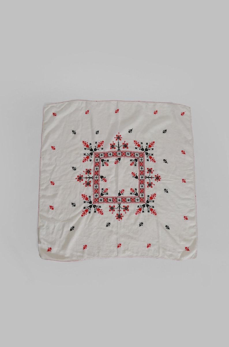 May include: White linen square tablecloth with red and black embroidered floral pattern.