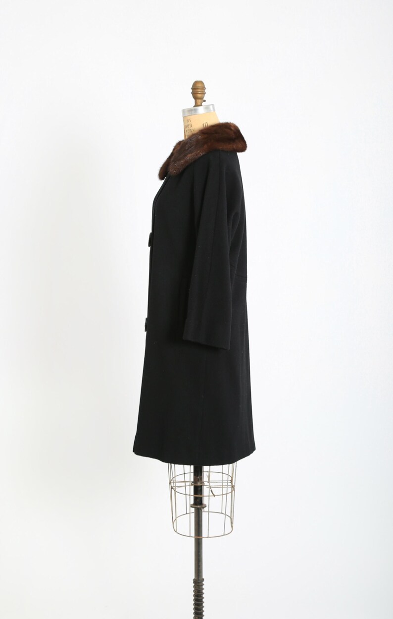 May include: A vintage black coat with a brown fur collar. The coat has a classic design with three buttons and three-quarter sleeves. The coat is displayed on a dress form.