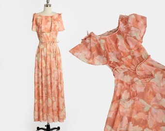 May include: A long, peach-coloured maxi dress with a floral print and a ruffled neckline. The dress has a tie at the waist and is made of a lightweight fabric.