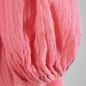 K&ouml;nnte beinhalten: Nahaufnahme eines rosa, strukturierten Stoffes, m&ouml;glicherweise ein &Auml;rmel oder Teil eines Kleidungsst&uuml;cks. Der Stoff scheint leicht zu sein und hat eine geknitterte oder geraffte Textur. Die Farbe ist ein weiches, ged&auml;mpftes Rosa.