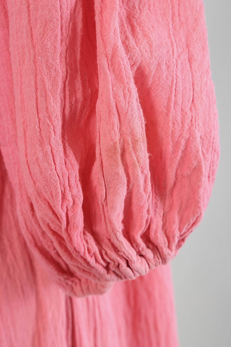 K&ouml;nnte beinhalten: Nahaufnahme eines rosa, strukturierten Stoffes, m&ouml;glicherweise ein &Auml;rmel oder Teil eines Kleidungsst&uuml;cks. Der Stoff scheint leicht zu sein und hat eine geknitterte oder geraffte Textur. Die Farbe ist ein weiches, ged&auml;mpftes Rosa.