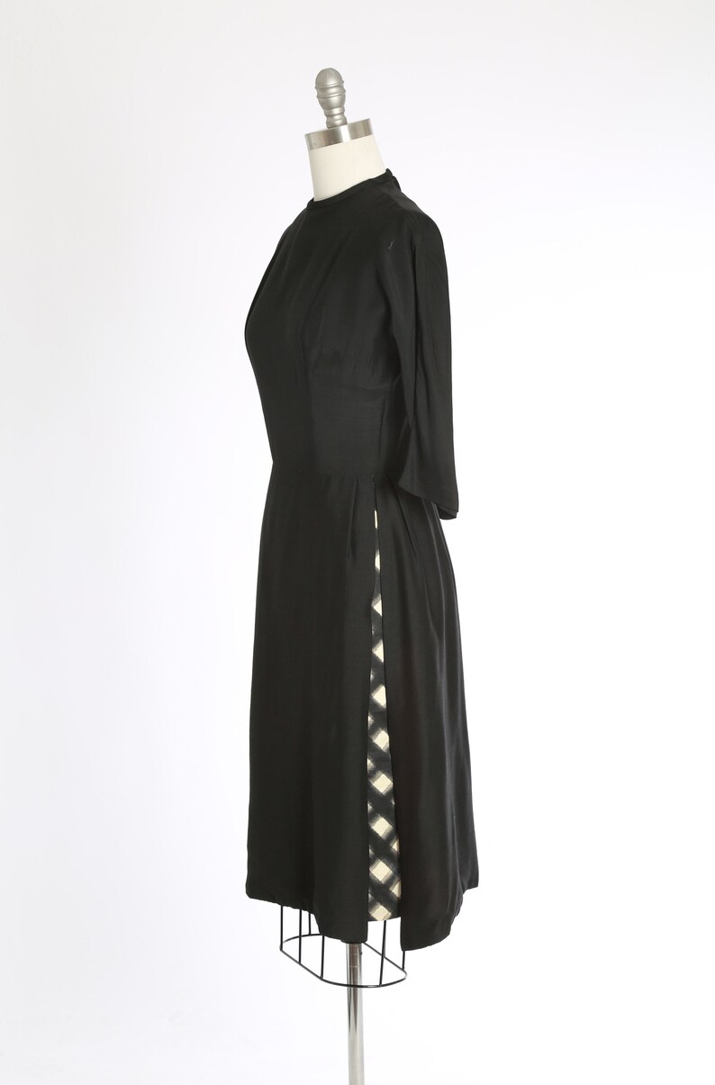 Puede incluir: Un vestido negro hasta la rodilla con un patr&oacute;n geom&eacute;trico blanco y negro en el lateral.