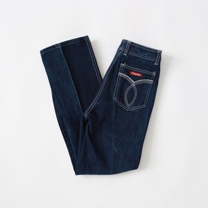 May include: A pair of dark blue denim jeans with white stitching detail. The jeans have a red label with the word "charisma" on the back pocket.