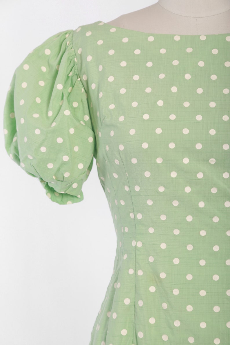 May include: A green dress with white polka dots and short puffed sleeves.