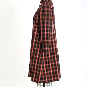 May include: A black and pink plaid dress with long sleeves and a mandarin collar. The dress is on a dress form.