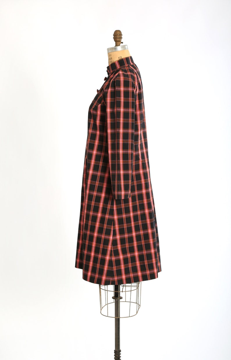 May include: A black and pink plaid dress with long sleeves and a mandarin collar. The dress is on a dress form.