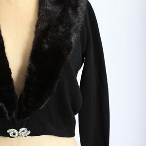 May include: A black cropped cardigan with a fur collar and a jeweled button closure.