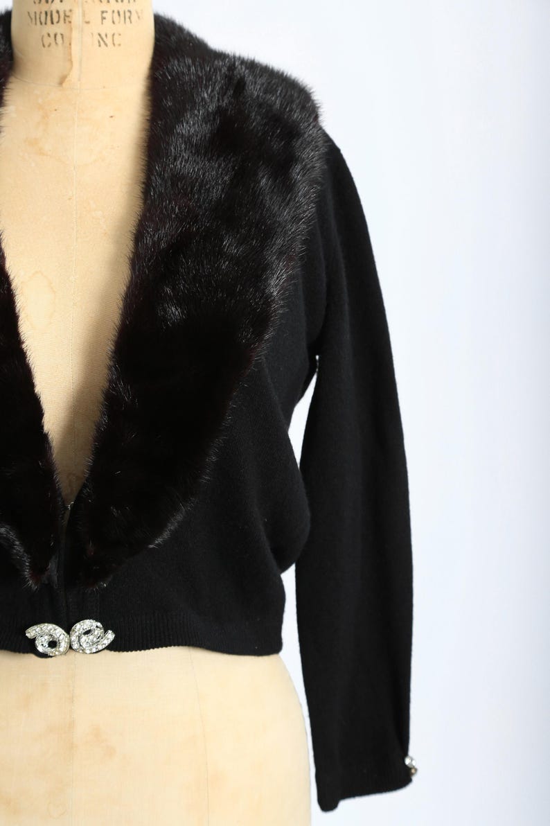 May include: A black cropped cardigan with a fur collar and a jeweled button closure.
