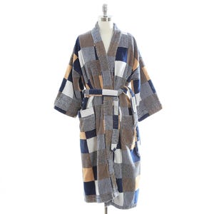 May include: A patchwork-style robe with a matching belt. The robe features a mix of blue, white, and tan squares and stripes. It has a shawl collar and two front pockets. The robe is displayed on a mannequin.