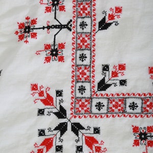 May include: White fabric with a black and red embroidered design. The design features a repeating pattern of geometric shapes and stylized flowers.
