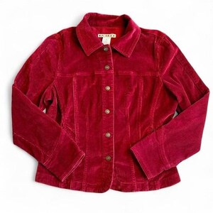 May include: A deep red corduroy jacket featuring a classic collar, long sleeves, and a front button-down closure with metallic buttons. The interior neck label displays the text A.M.I. The garment has vertical seam detailing and a textured fabric finish.