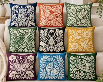 May include: A collection of nine square throw pillows featuring cream-colored nature-themed illustrations on solid backgrounds. Designs include an owl, butterfly, hummingbird, sea turtle, beetle, birds, moth, fox, and rabbit, all framed by foliage.